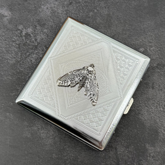 Silver moth cigarette case with dark recessed details and geometric metal background