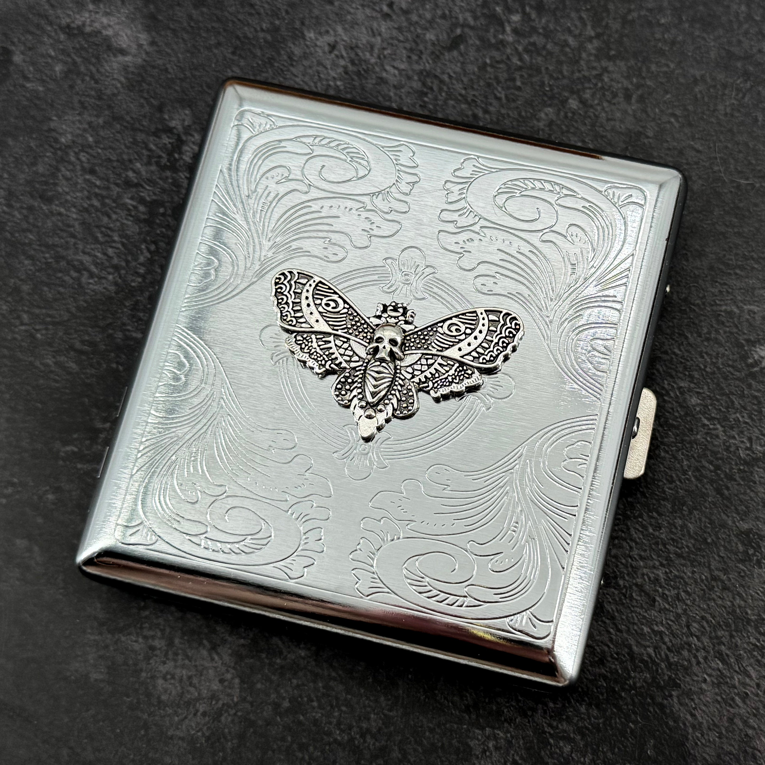 Silver Death's-head hawkmoth metal cigarette case with ornate stamped scrollwork background