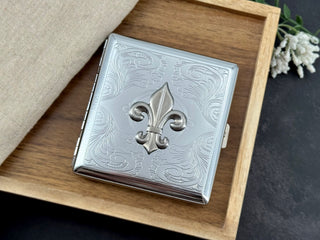 Ornate silver metal cigarette case with raised fleur-de-lis centerpiece