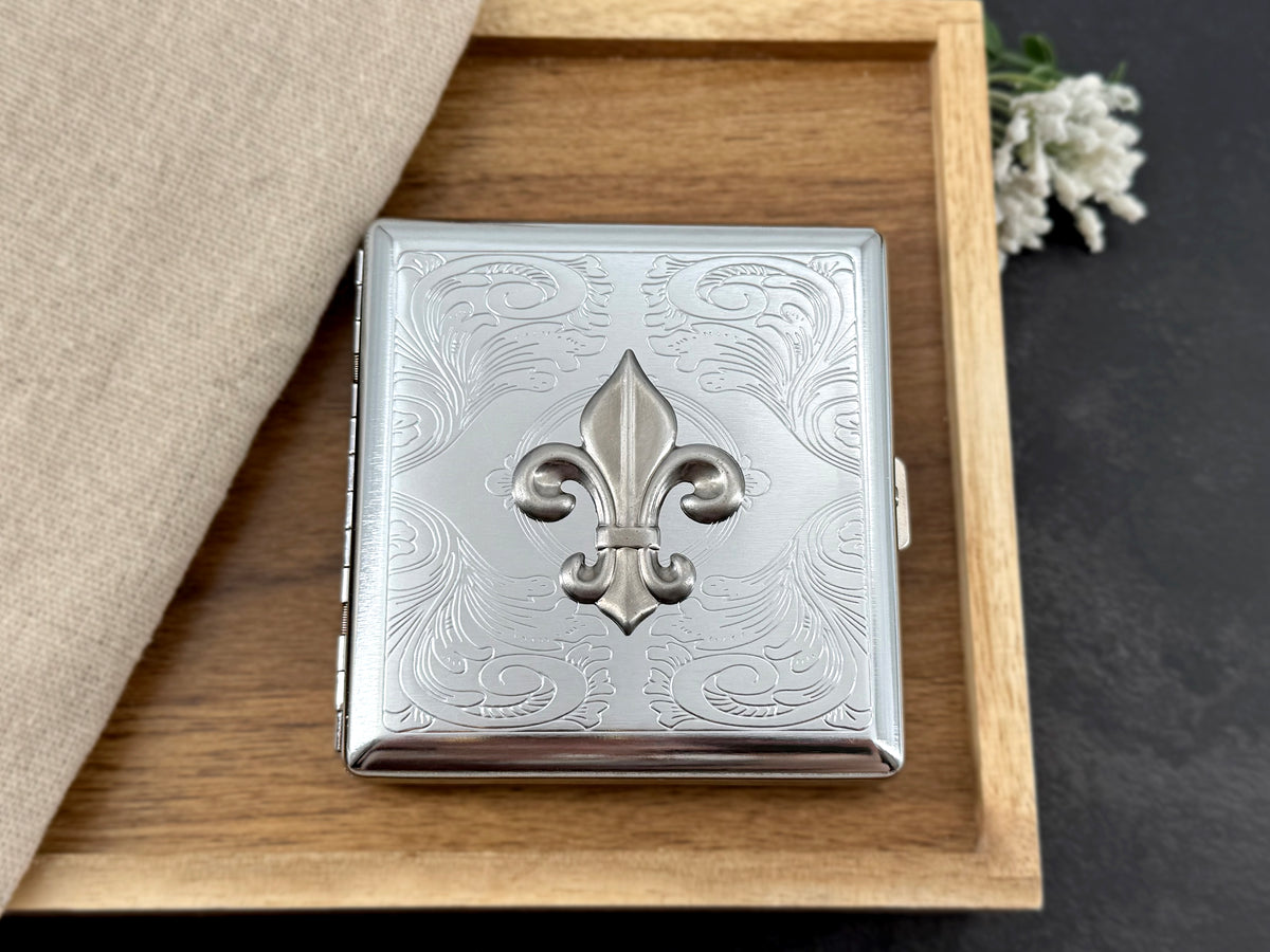 Silver cigarette case with decorative scrollwork and fleur-de-lis design