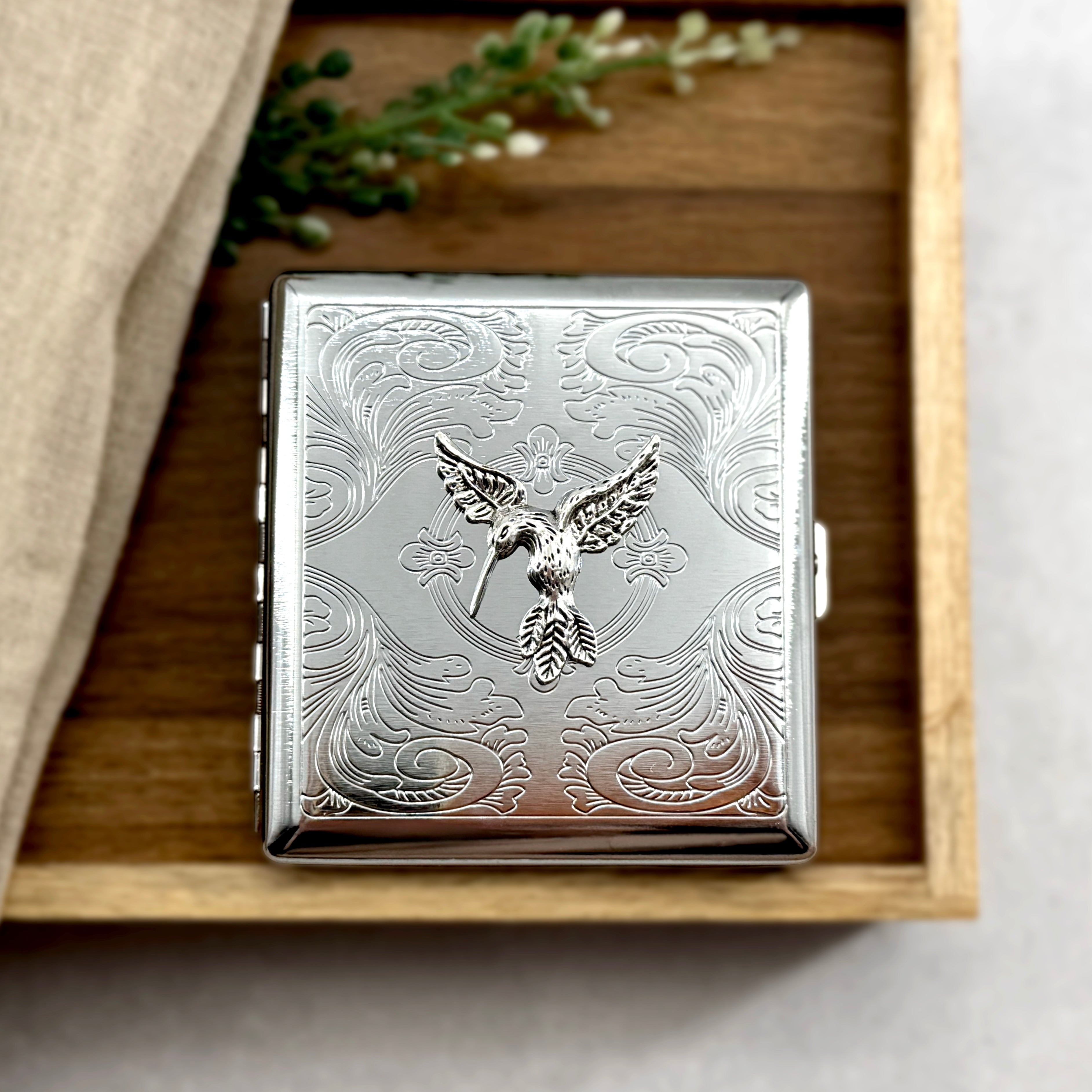Nature-inspired cigarette case with raised hummingbird accent and decorative engraved background