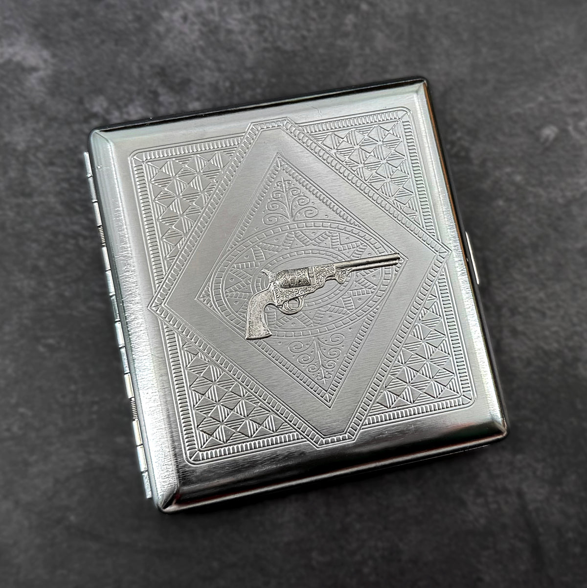 Handmade silver metal cigarette case featuring a raised silver-toned revolver.