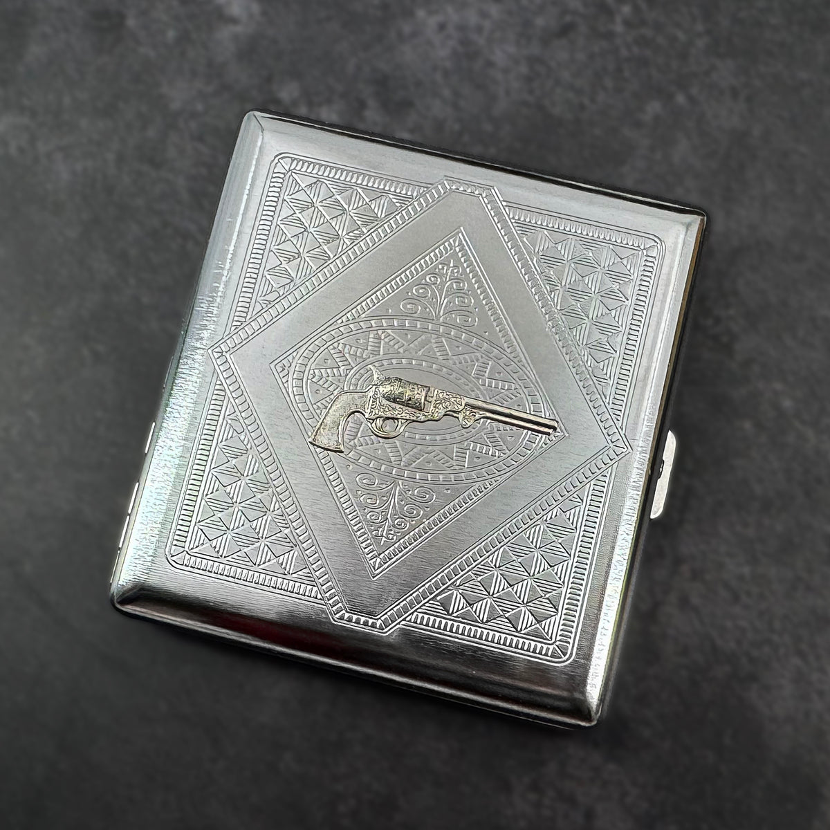 Angled view of silver revolver cigarette case showing raised pistol design.