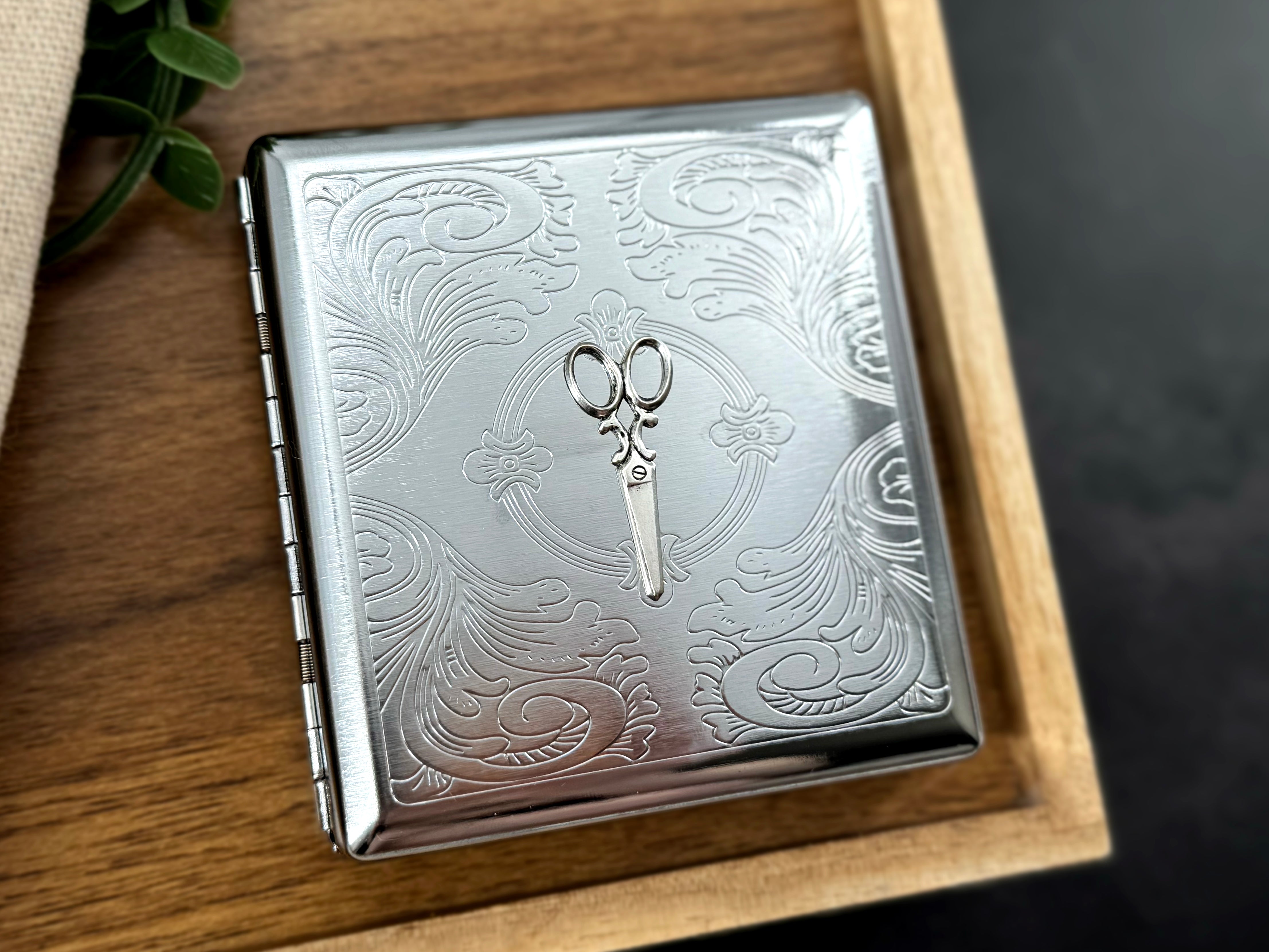 Decorative silver scissors metal case with intricate stamped floral scrollwork and secure snap closure