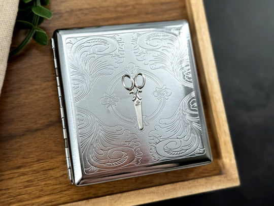 Decorative silver scissors metal case with intricate stamped floral scrollwork and secure snap closure
