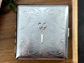 Close-up of raised scissors embellishment on a handcrafted silver metal cigarette case