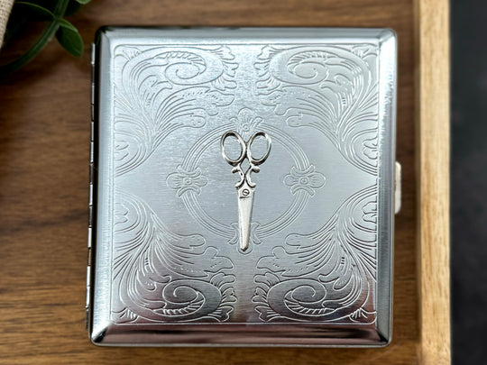 Close-up of raised scissors embellishment on a handcrafted silver metal cigarette case