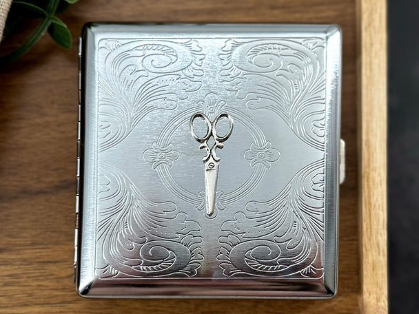 Close-up of raised scissors embellishment on a handcrafted silver metal cigarette case