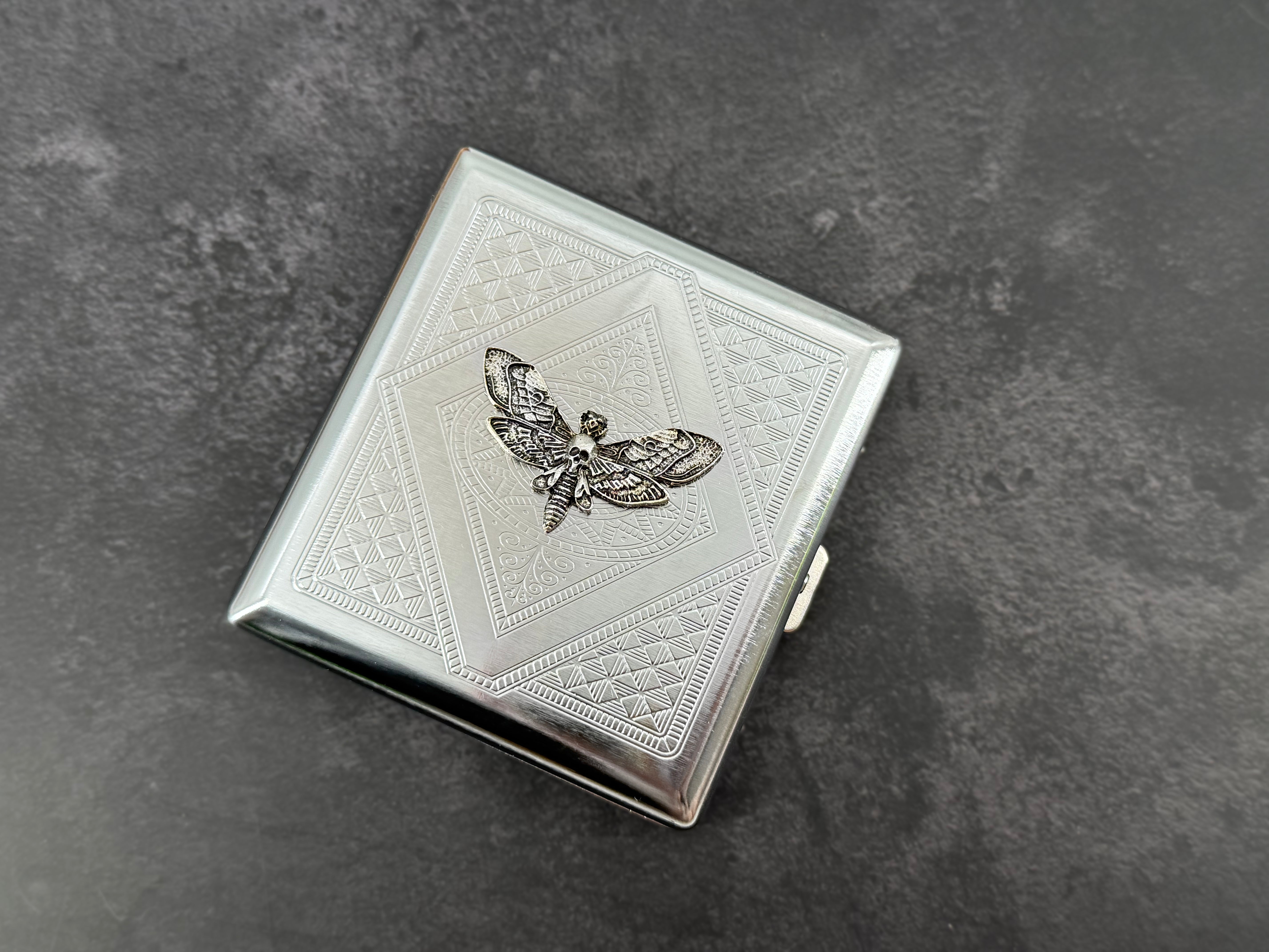 Silver moth cigarette case with dark recessed wing details and stamped metal pattern