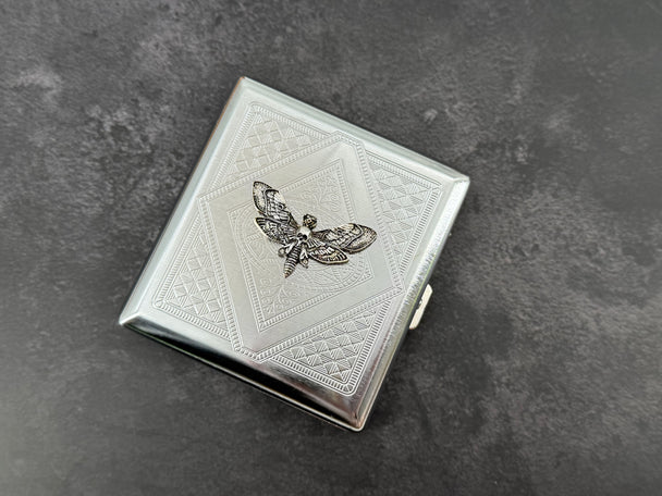 Silver moth cigarette case with dark recessed wing details and stamped metal pattern
