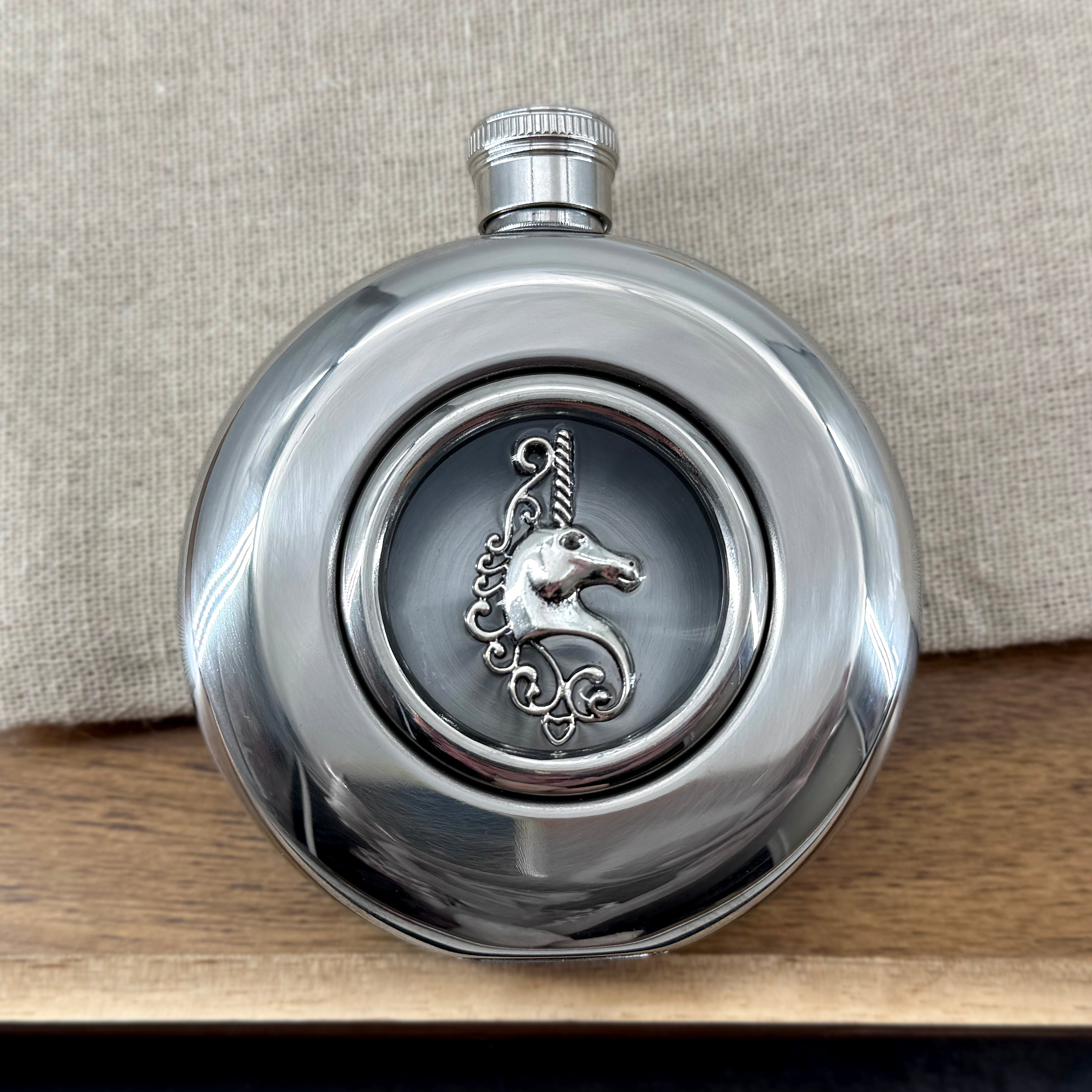 Round stainless steel flask with raised silver unicorn and clear circular viewing window