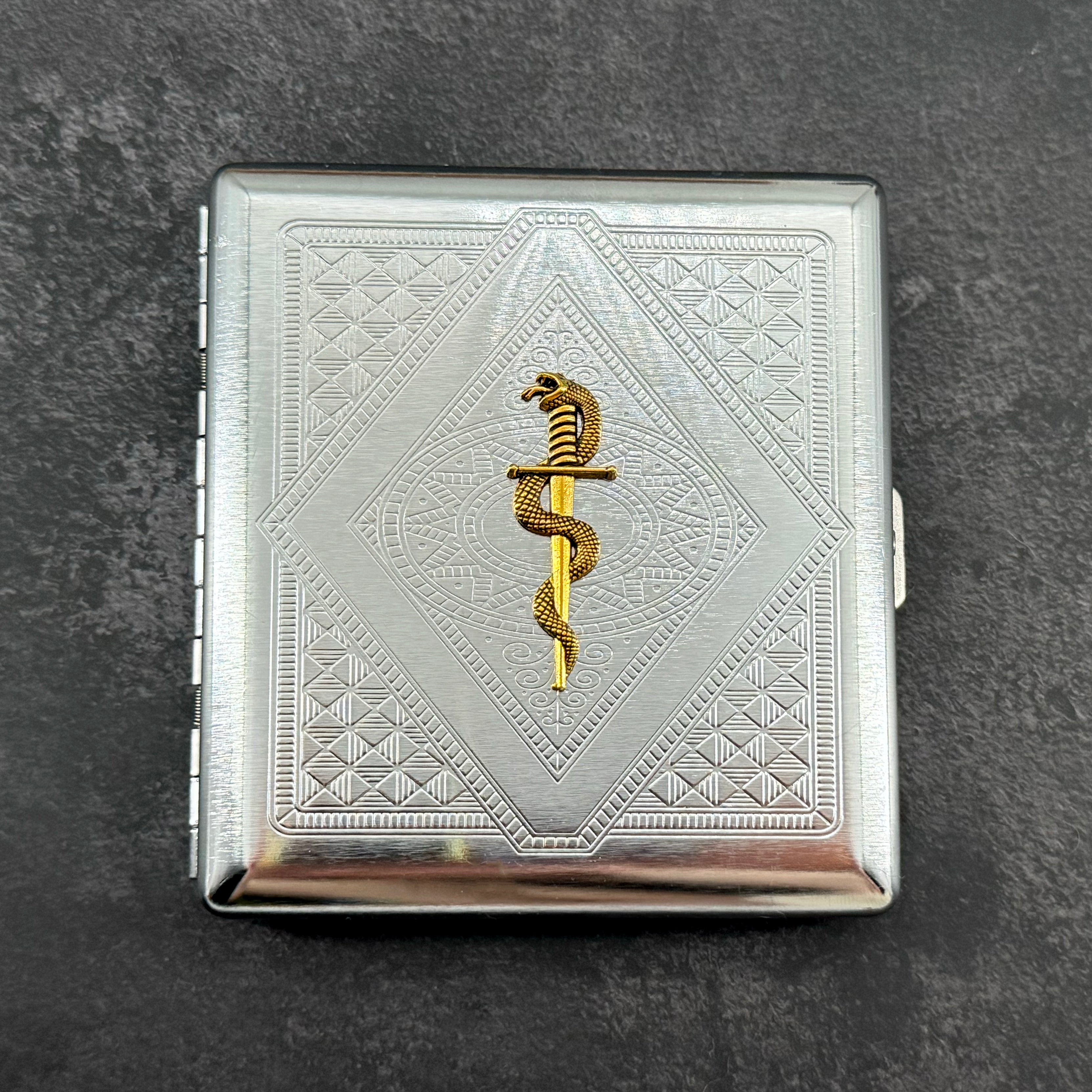 Snake and Blade cigarette case with raised gold serpent and dagger on silver stamped metal background