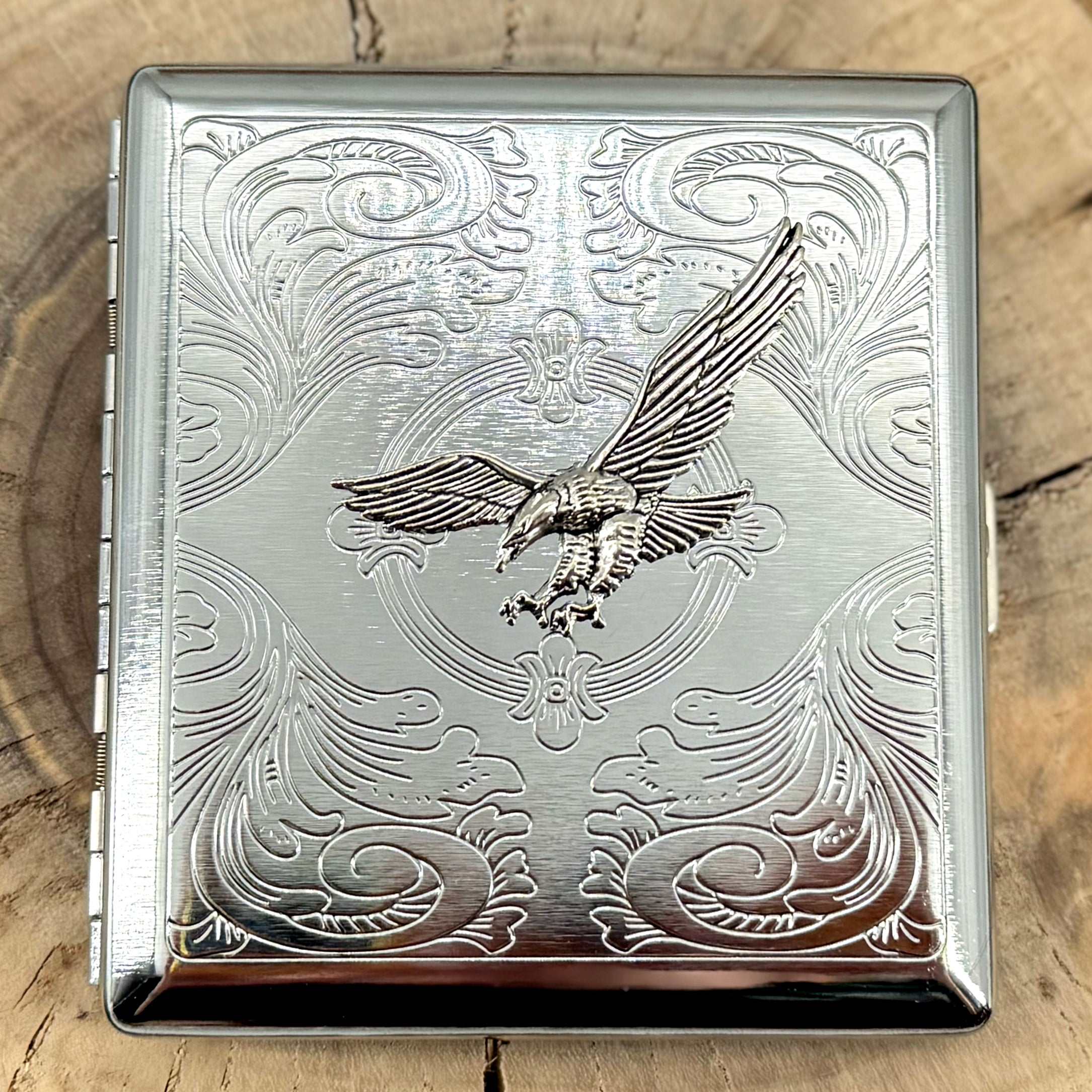 Silver metal cigarette case featuring raised soaring eagle on engraved scrollwork
