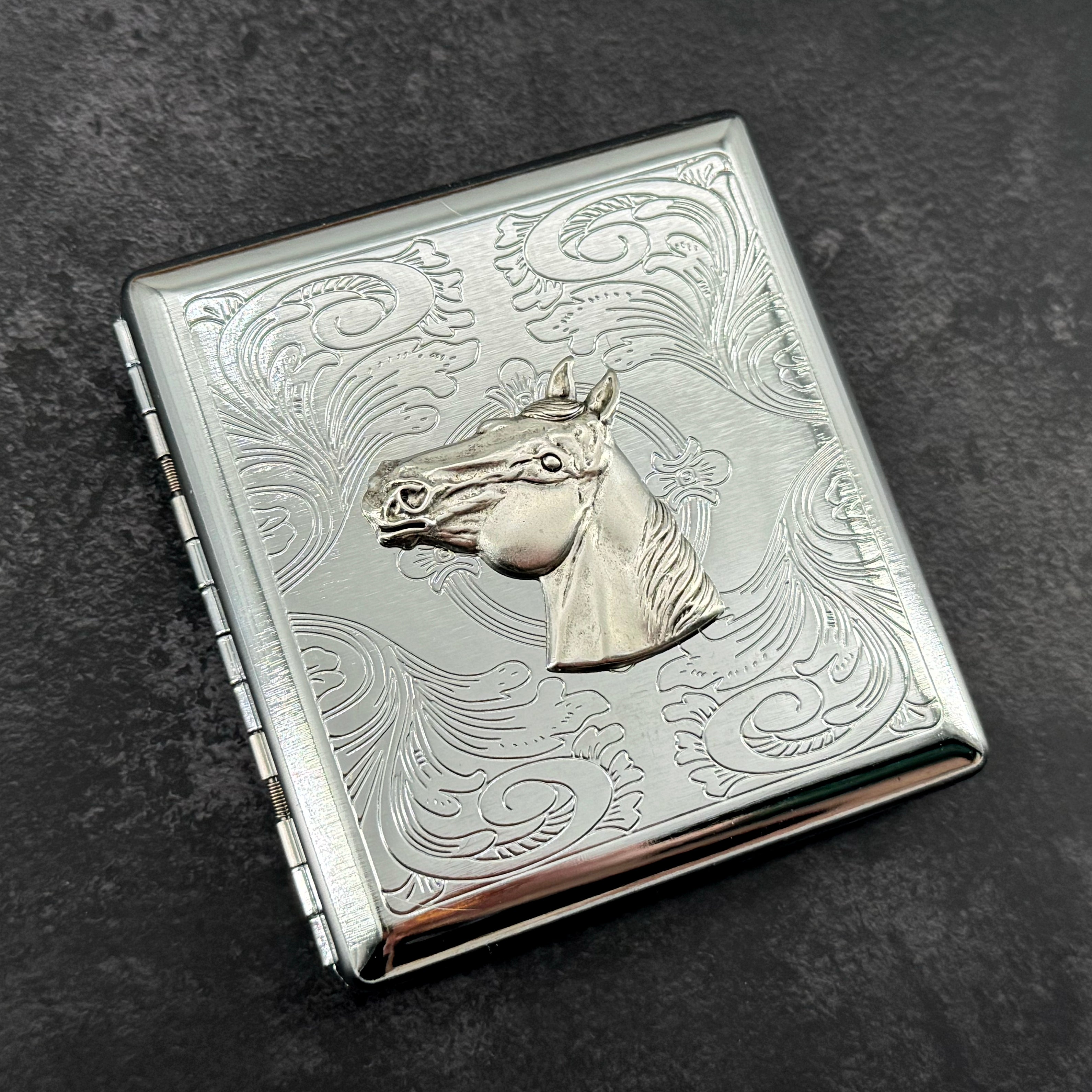 Silver stamped metal cigarette case with raised horse head and ornate scrollwork
