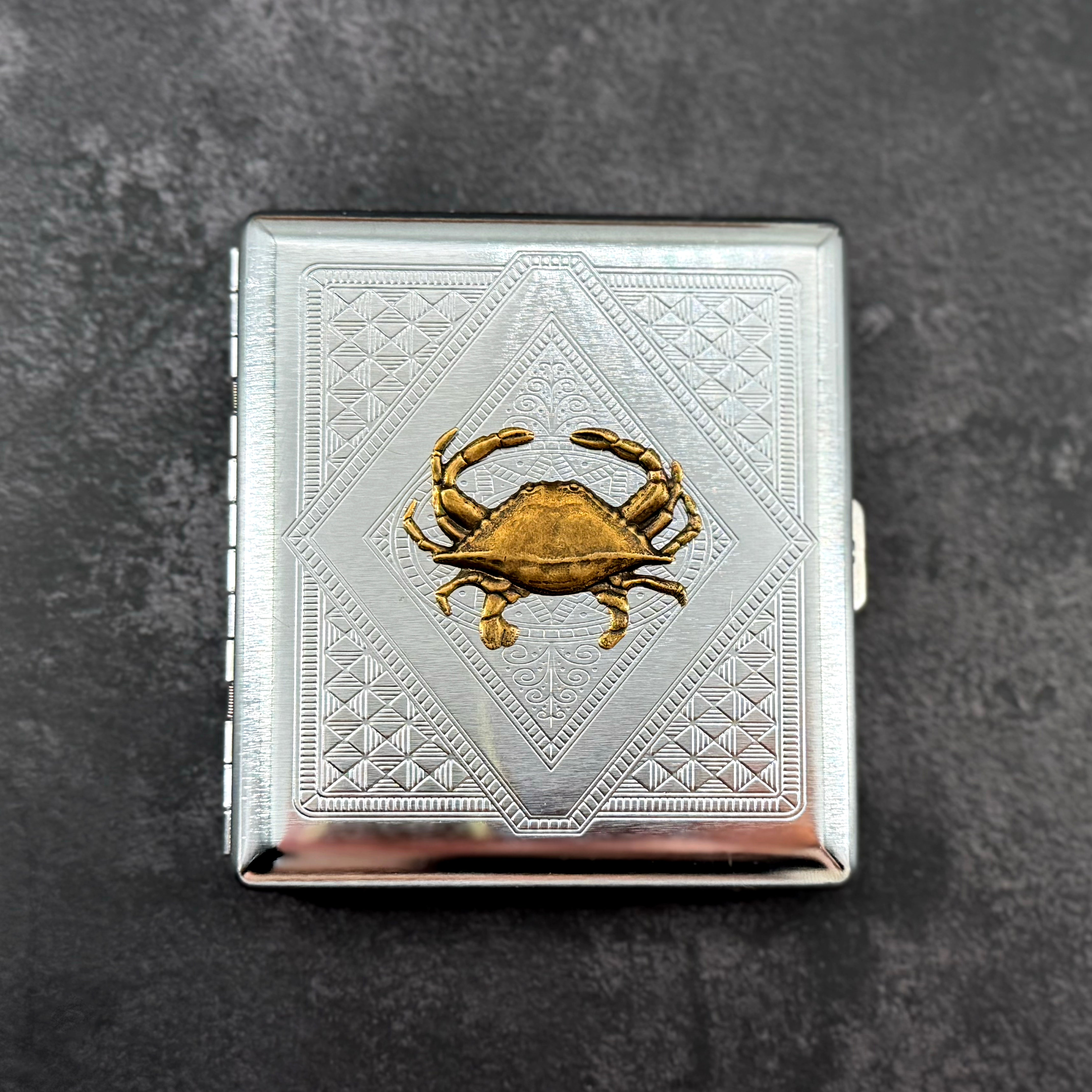 Crab cigarette case with raised bronze crab on silver stamped metal background