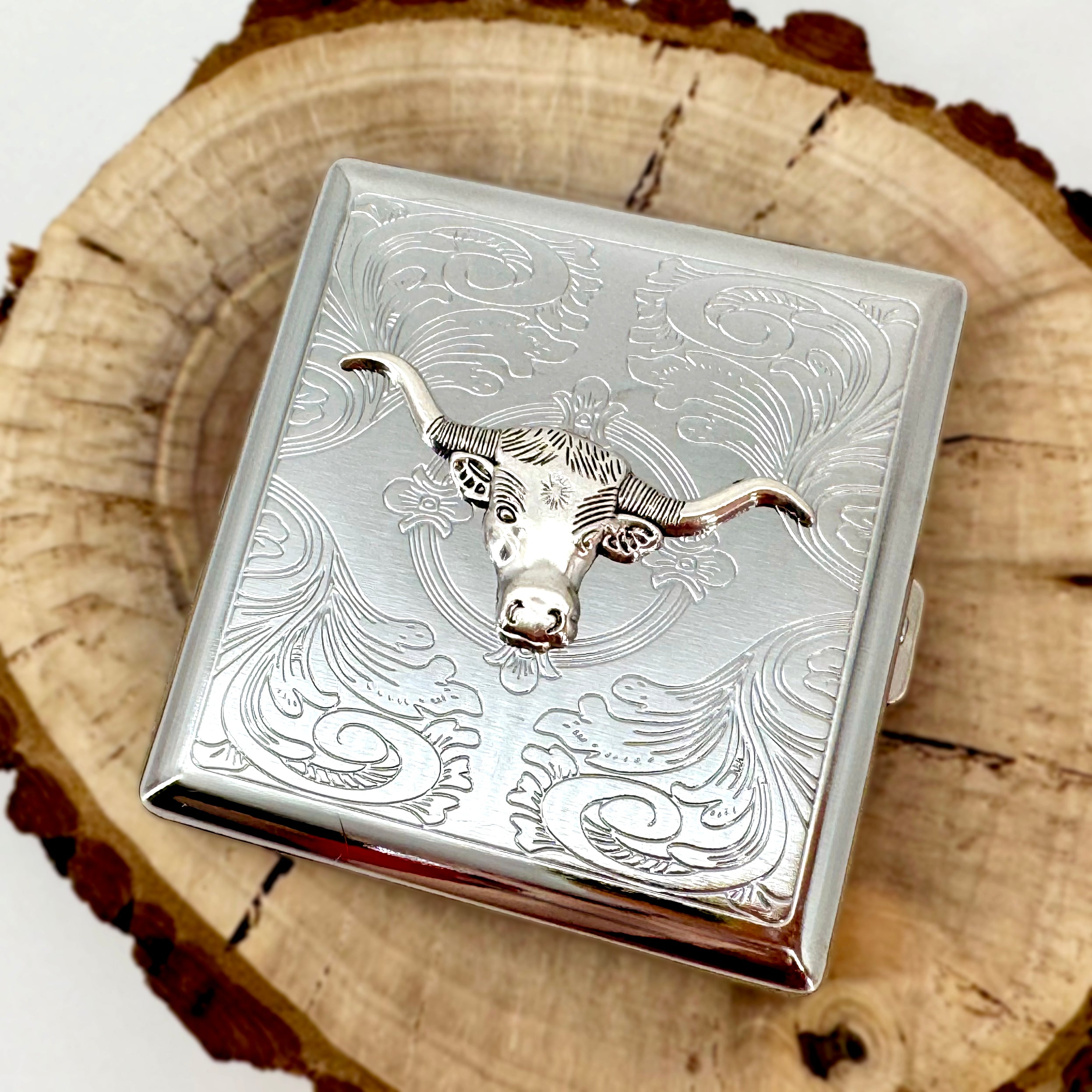 Western longhorn cigarette case with raised cattle emblem and engraved ornamental background