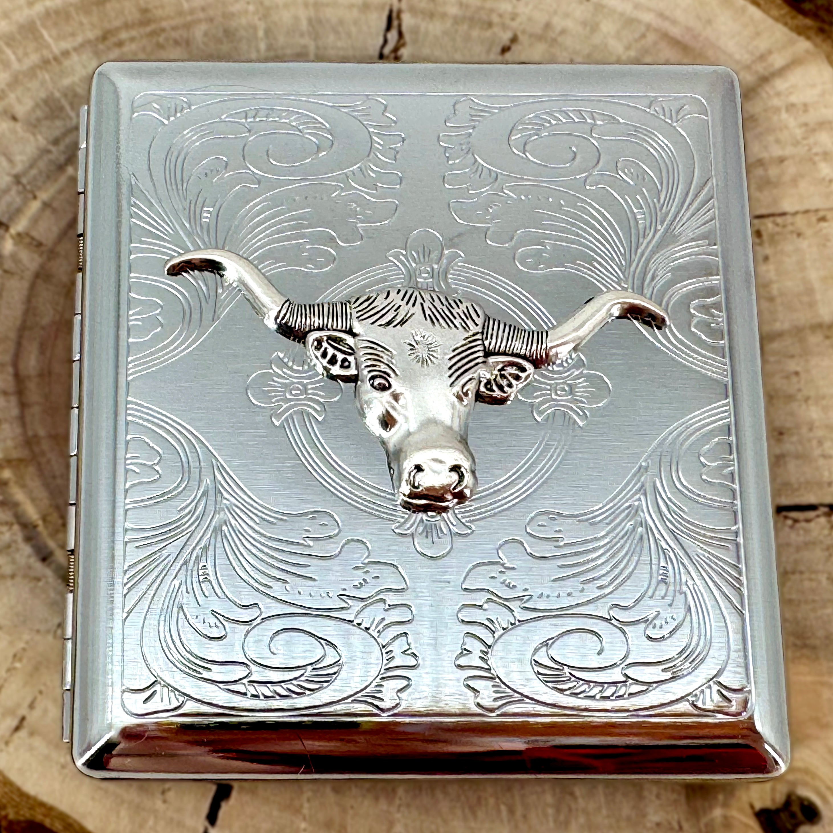 Western longhorn pocket case displayed on a natural wood slice with engraved silver finish