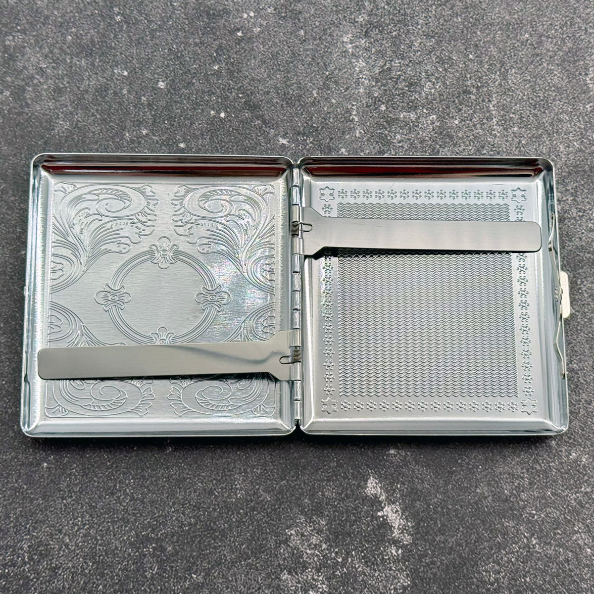 Open fleur-de-lis cigarette case showing interior retaining arms